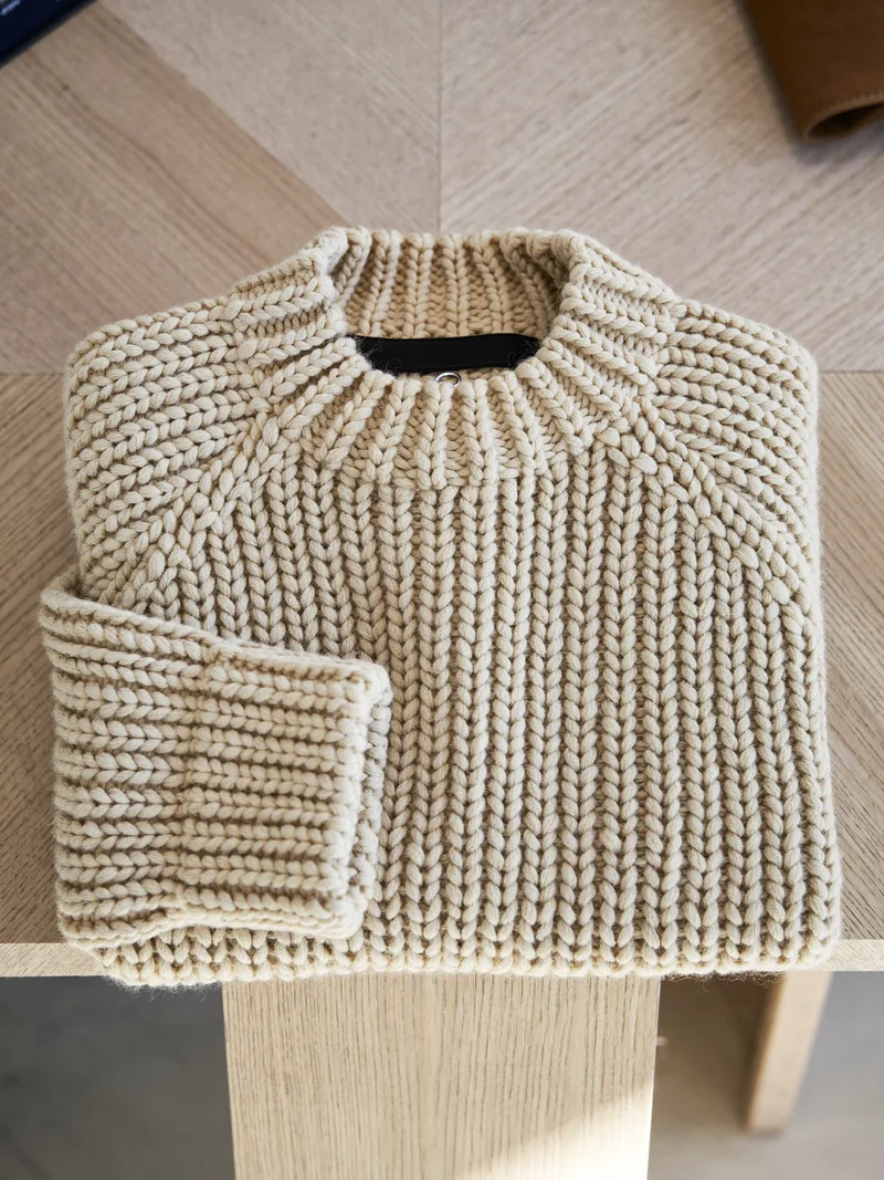 Grobstrickpullover in Hafer, flach auf heller Eiche gefaltet, Illustration